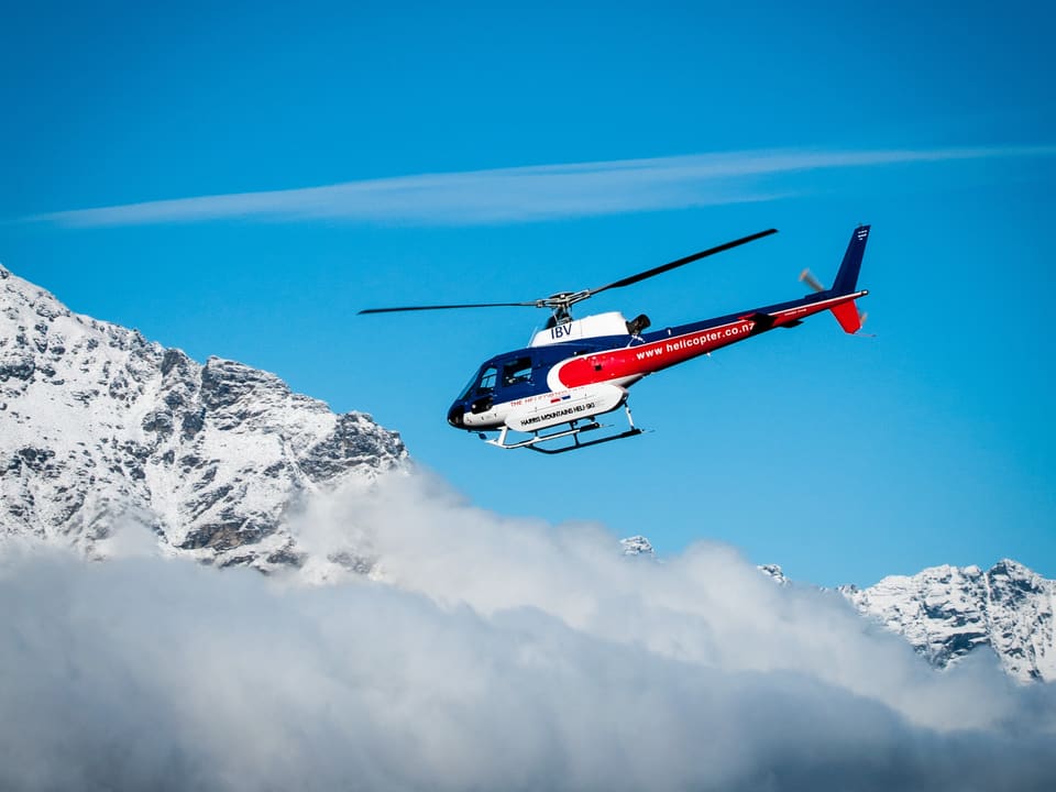 A helicopter flying above the clouds beside snow peaks